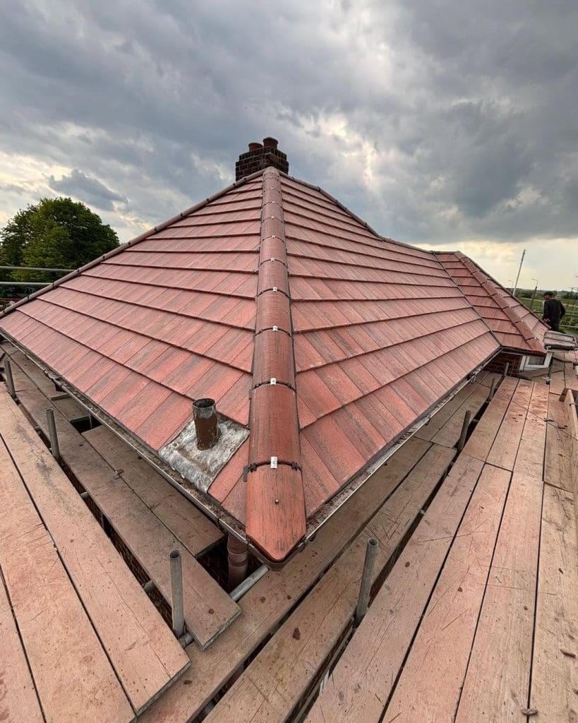 A red-tiled roof with a central chimney and a small vent, surrounded by wooden scaffolding under a cloudy sky.